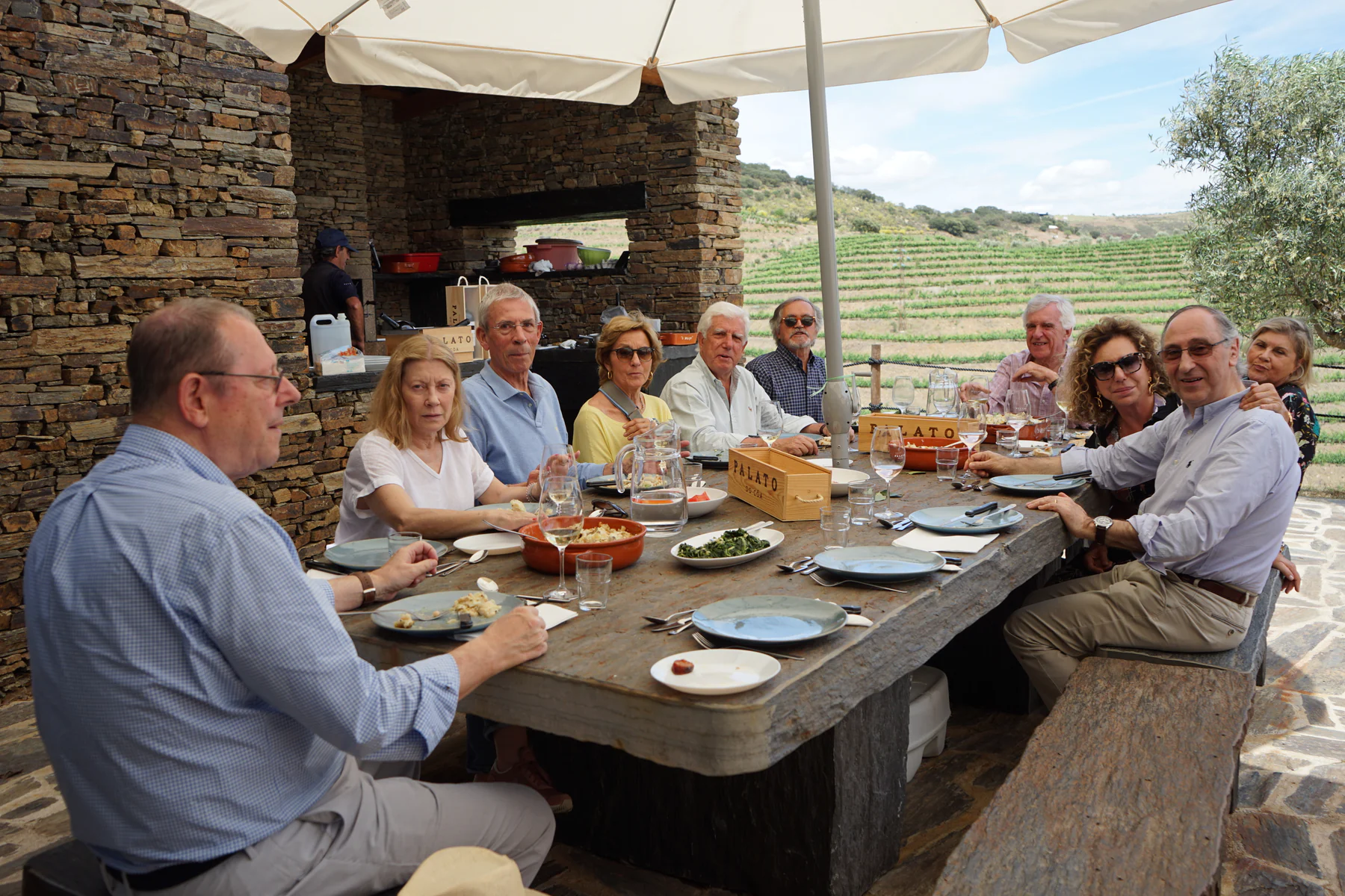 Friends gathered for lunch at the stone table, facing the vineyard