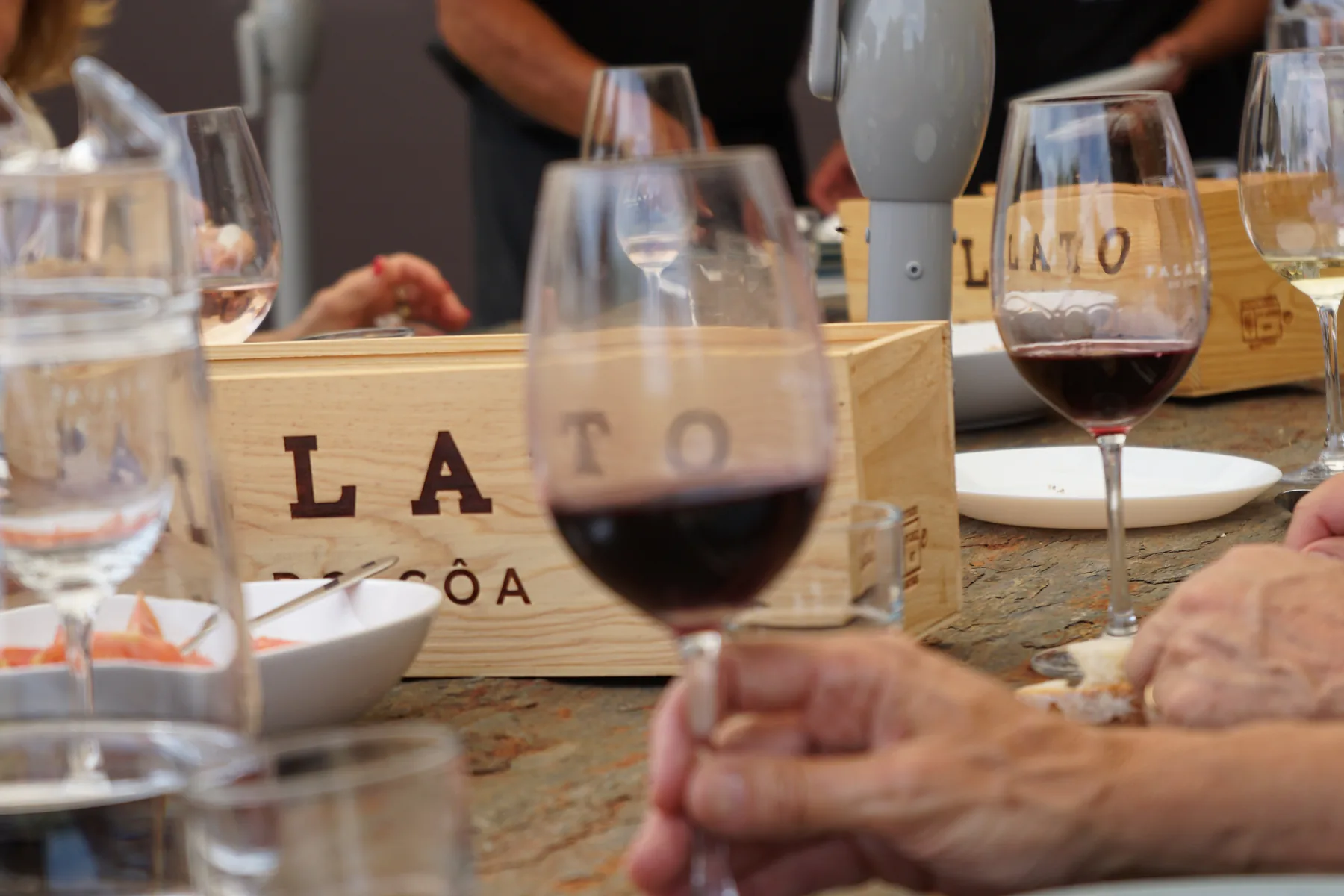 Um copo de tinto à mesa de xisto, com a caixa Palato e os pratos